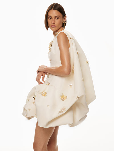 Model is wearing a white dress with gold and pearl floral embroidery scattered across the dress. 