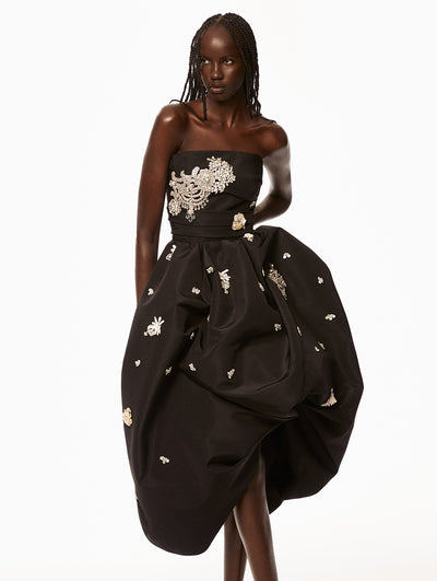 Model is wearing black dress with silver and pearl floral embroidery scattered across the dress. 