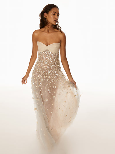 Model is wearing ivory dress with floral detailing cascading down the dress. The model is wearing gold floral earrings. 