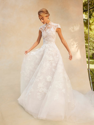 The model wears a short sleeve lace wedding gown with a high neck and transparency detail in the shoulder area.