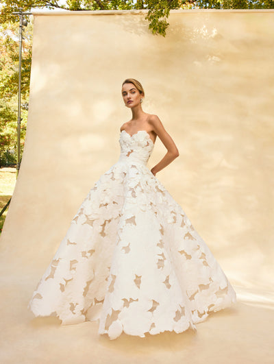 The model is wearing a strapless wedding gown with embroidered flowers all over. Front view