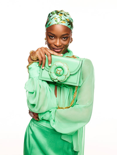 A model poses against a white backdrop in an Oscar de la Renta green blouse and skirt with a matching green handbag. 