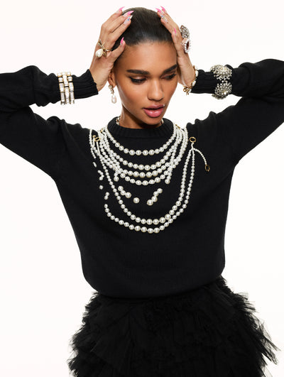 A model poses against a white backdrop in an Oscar de la Renta black sweater with pearl detailing. 