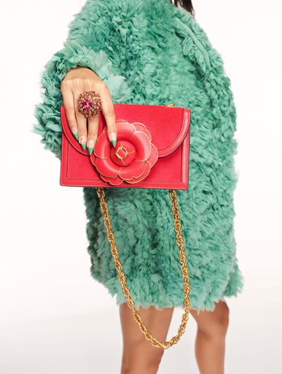 A model poses against a white backdrop in an Oscar de la Renta green faux fur coat styled with an orange handbag. 