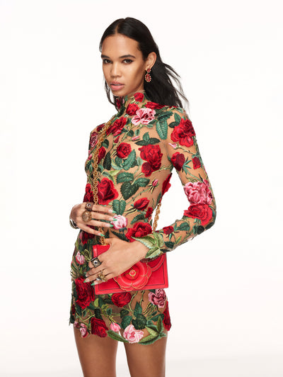 A model poses against a white backdrop in an Oscar de la Renta floral embroidered cocktail dress.