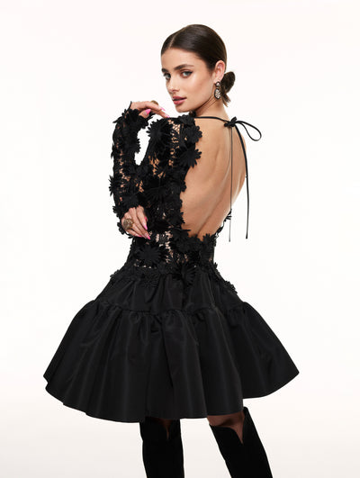 A model poses against a white backdrop in an Oscar de la Renta black lace cocktail dress.