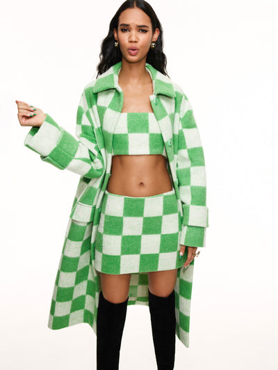 A model poses against a white backdrop in an Oscar de la Renta green checkered coat and matching crop top and skirt set. 