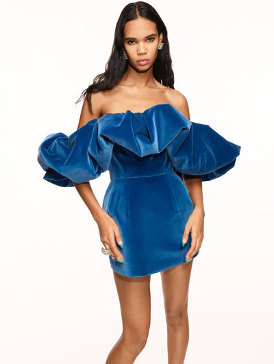 A model poses against a white backdrop in an Oscar de la Renta blue velvet cocktail dress.