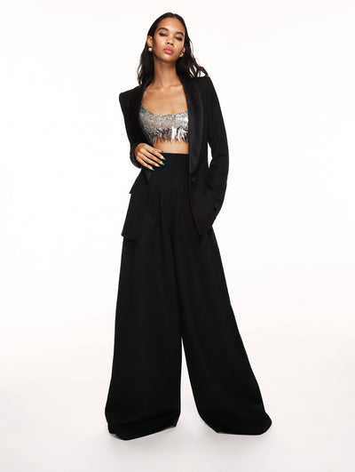A model poses against a white backdrop in an Oscar de la Renta black pant suit with a silver sequin fringe bralette top. 