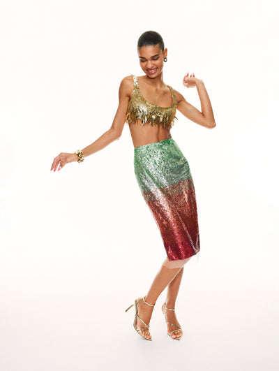 A model poses against a white backdrop in an Oscar de la Renta gold sequin fringe bralette top and ombre sequin skirt. 