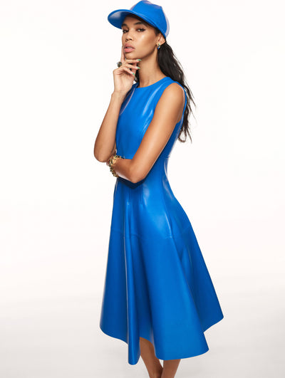 A model poses against a white backdrop in an Oscar de la Renta blue leather dress and matching ball cap hat. 