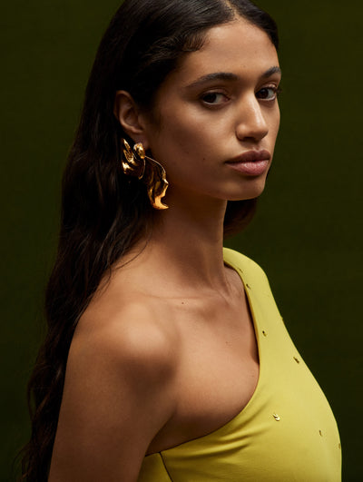 The model is wearing gilded hoop earrings which have been sculpted into a form reminiscent of a flower.