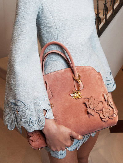 The model wears a tweed light blue mini dress paired with a blush suede floral tote bag. The dress features long sleeves and embroidery at the bottom. 