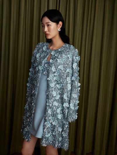 The model wears a light blue embroidered cocktail dress with a matching long sleeve coat.  