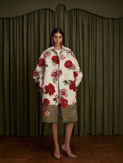The model is wearing a white jacquard coat with red floral motifs. 