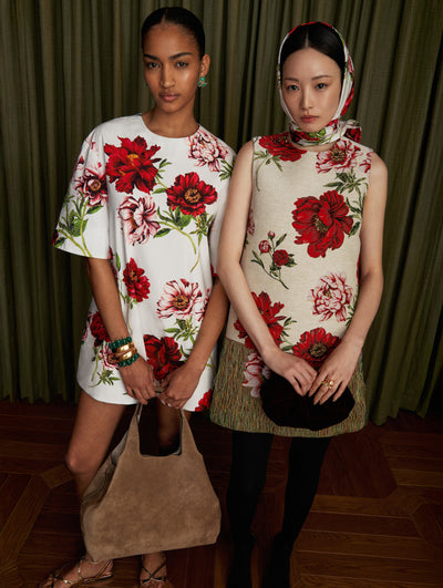 Two models stand next to each other. The model on the left is wearing a white short sleeve shirt dress with red floral motifs. The model on the right is wearing a sleeveless jacquard red floral motif. 