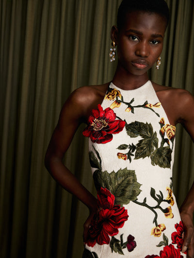 The model is wearing a floral embroidered halter neck gown with fringe detailing at bottom.  