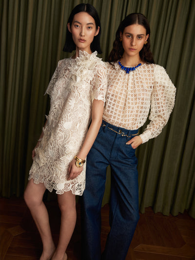 The model is wearing a white short sleeve lace guipure mini day dress. The model is wearing a white long sleeve lace guipure blouse with dark denim jeans. 