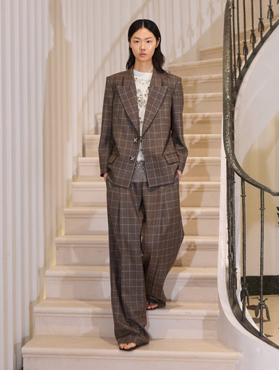 The model is wearing a grey and blue plaid suit set paired with a crystal embroidered white t-shirt. The look is styled with a black clutch.  