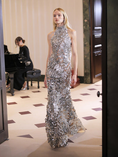 The model wears a halter neck silver embroidered gown.  