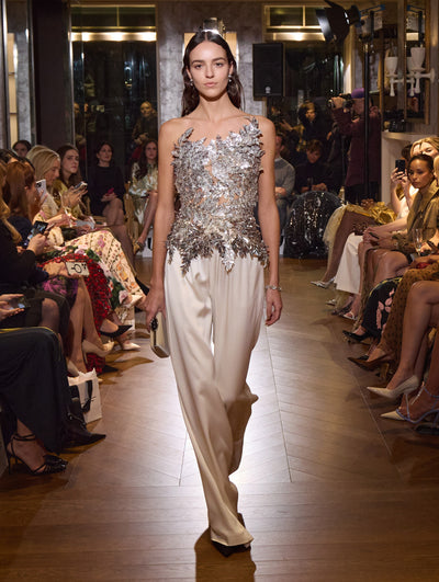 The model wears a strapless silver embroidered top with white sequin trousers.  
