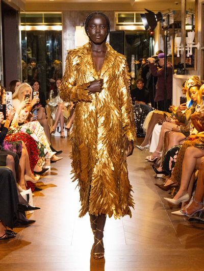 The model wears a statement gold coat with feature detailing.  