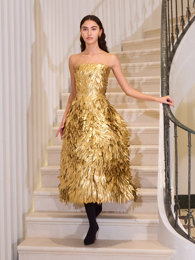 The model wears a statement strapless cocktail dress with feather detailing.  