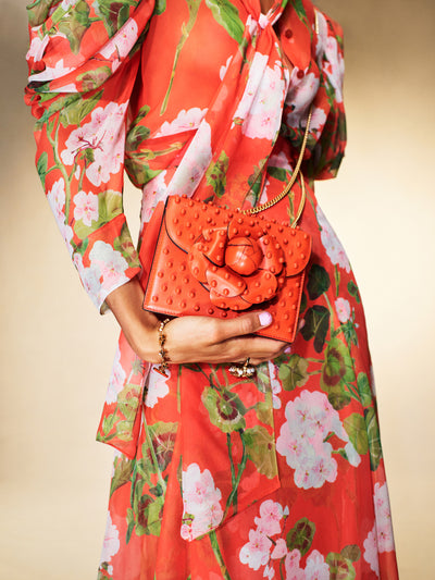The model is carrying a red handbag with a large flower at the clasp and bubble details throughout. 