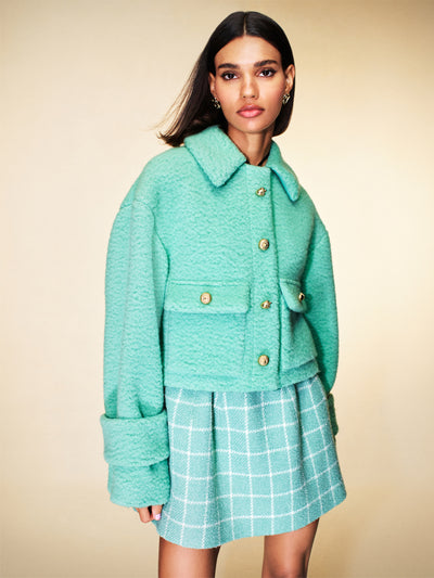 The model is wearing a baby blue tweed jacket with a blue and white checkered tweed skirt. 
