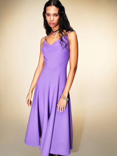 The model is wearing a purple midi dress with a cowl neckline. 