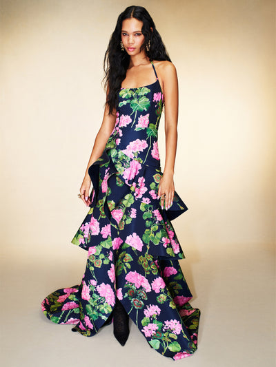 The model is wearing a navy halter-neck evening gown with ruffles and pink floral detailing. 