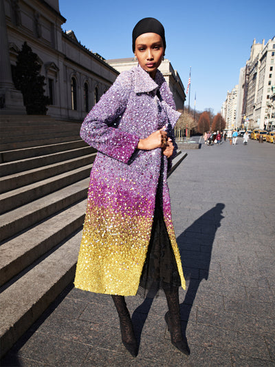 The model is wearing an ombre sequin coat, ranging from silver to lilac to gold. 