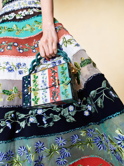 The model is carrying a multicolored floral purse with a teal chain handle. 