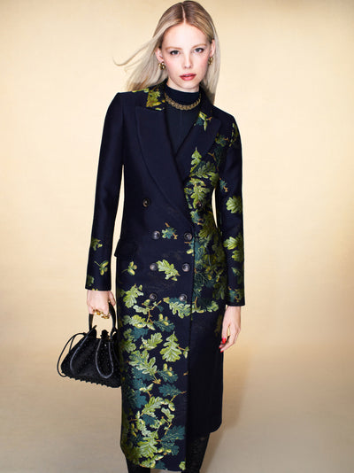 The model is wearing a navy peacoat with green embroidered leaves scattered throughout. 