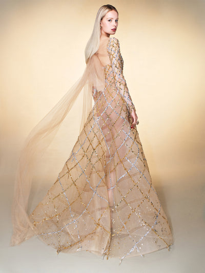 The model is wearing a beige evening dress with a gold and silver checkered pattern and a large tulle bow. 