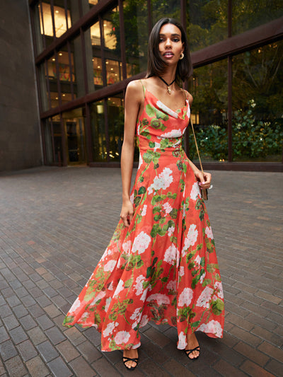 The model is wearing a sleeveless red evening dress with large green and white flowers. 