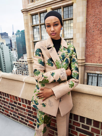 The model is wearing a brown pantsuit with green leaves embroidered throughout. 