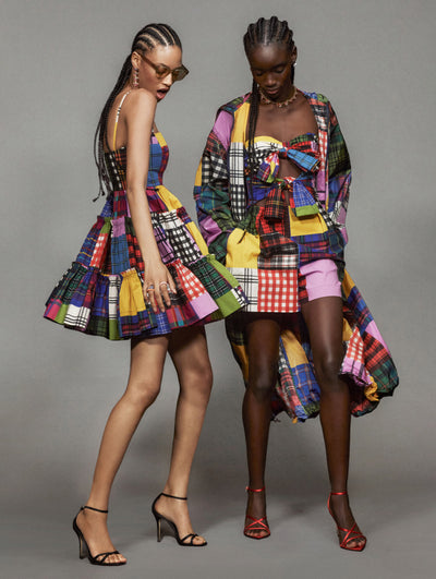 Two models pose in Oscar de la Renta ready-to-wear looks against a grey back drop. One model is wearing a plaid mini dress and the other is wearing a plaid romper and jacket. 