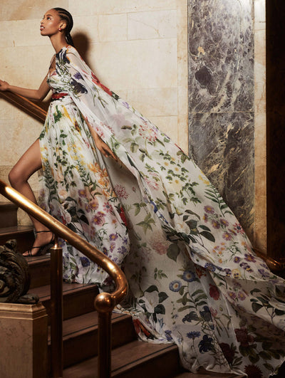 A model walks up a flight of stairs in an Oscar de la Renta floral gown with a matching cape. 
