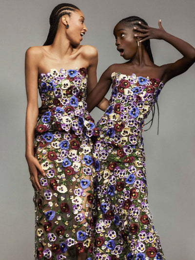 Two models pose against a grey backdrop in Oscar de la Renta floral embroidered gowns. 