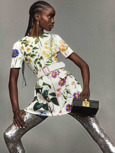 A model poses against a grey backdrop in an Oscar de la Renta white belted day dress with silver sequin tights. 