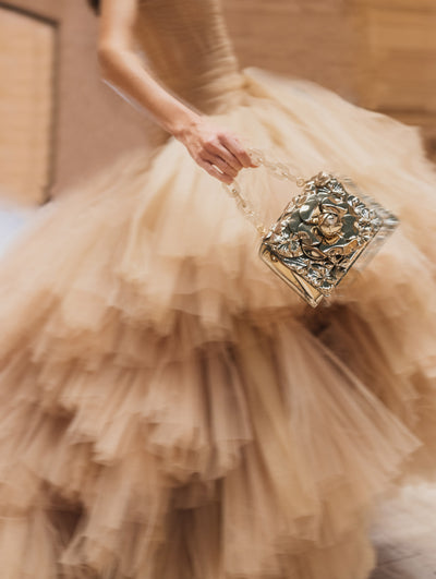 A model poses in an Oscar de la Renta beige tulle dress with a metallic handbag. 