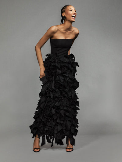 A model poses against a grey backdrop in an Oscar de la Renta black strapless gown. 