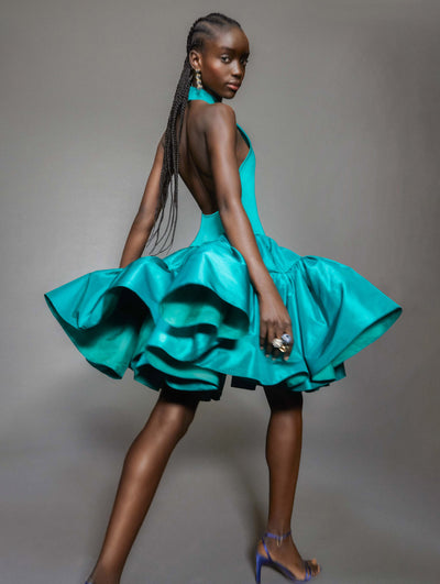 A model poses against a grey backdrop in an Oscar de la Renta teal cocktail dress.