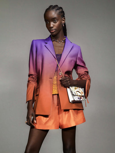 A model poses against a grey backdrop in an Oscar de la Renta ombre jacket and short set. 