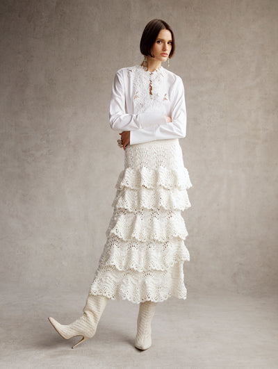 The model is wearing a white blouse with a white crochet midi skirt with a ruffle trim. 