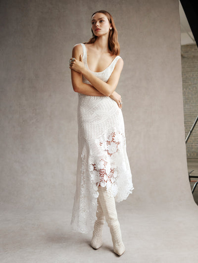 The model is wearing a white crochet midi dress with white boots. 