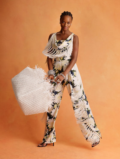 The model is wearing a silk navy top and pant set with large white flowers and white fringe. 