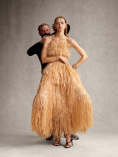 The model is wearing a strapless fringe midi dress with an exaggerated skirt shape. 