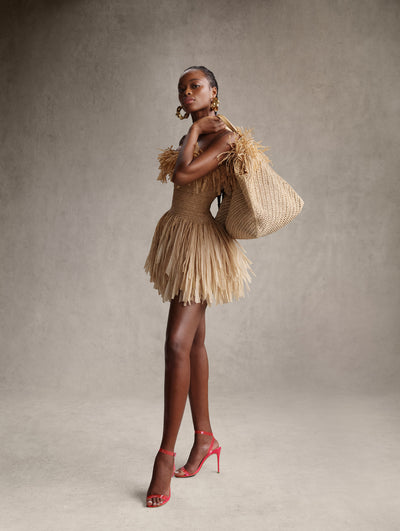 The model is wearing a rattan mini dress with a rattan purse. 